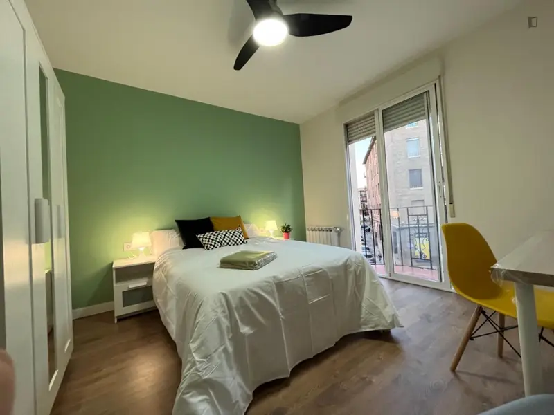 Habitación muy luminosa con balcón, frigorífico, Smart TV y ventilador de techo.